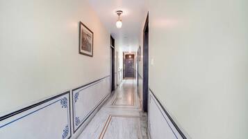 Um corredor com piso de mármore, obras de arte nas paredes e luminária no teto.