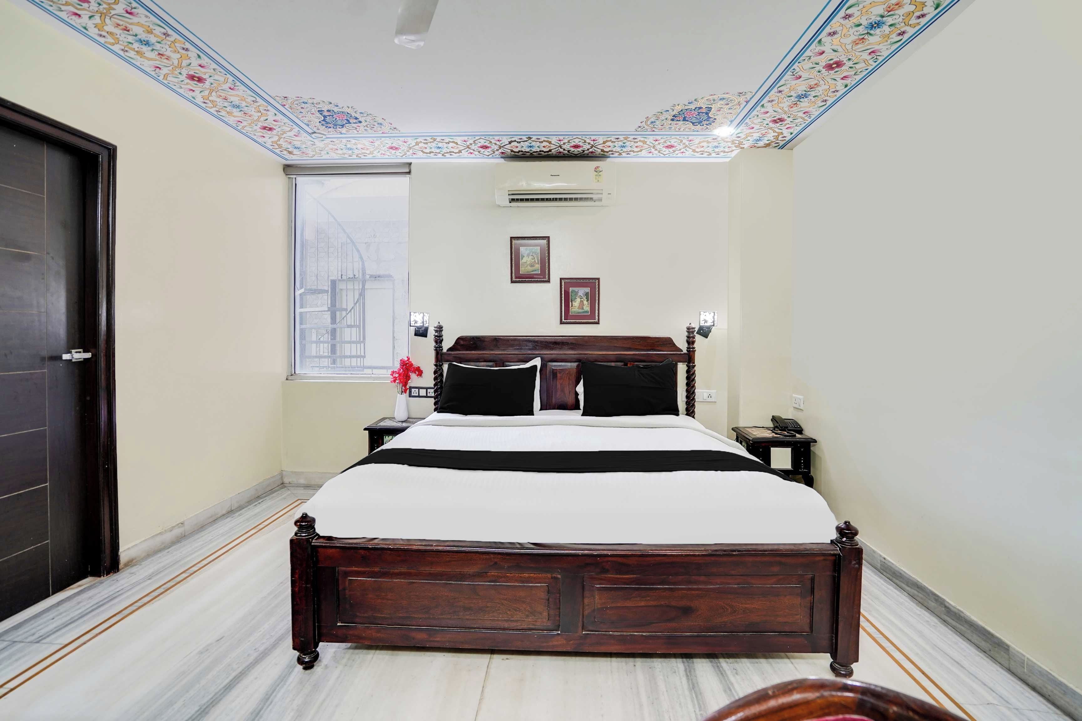 Quarto com cama grande, mesa de cabeceira, ar-condicionado fixado na parede e janela com vista.