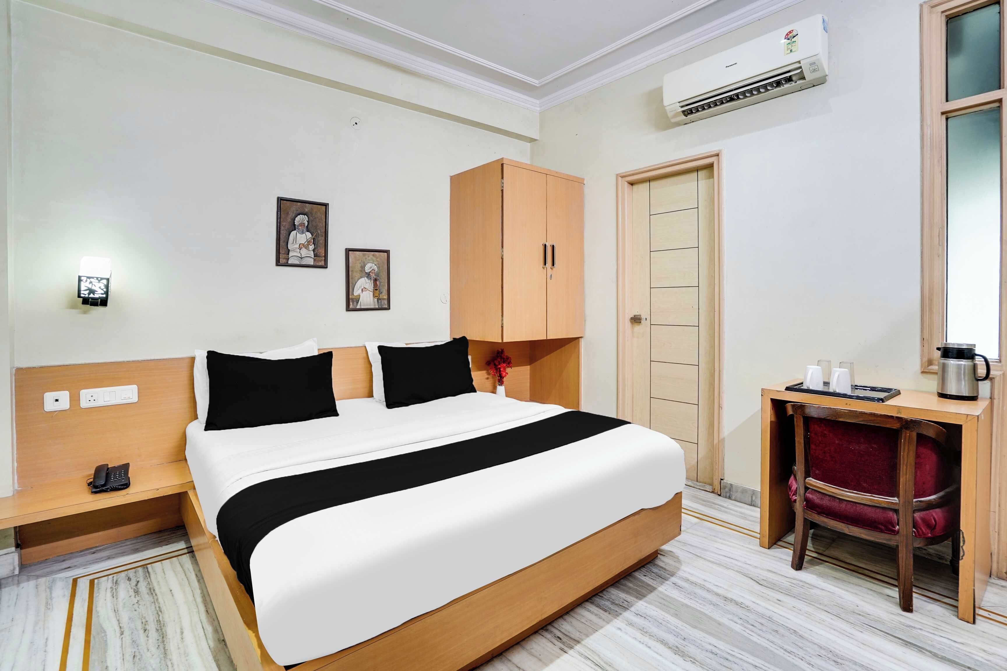 Habitación de hotel con cama, escritorio, silla, aire acondicionado y puerta.