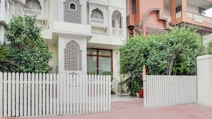 A gated entrance to a building with a white picket fence, a staircase leading to a door with a window, and lush greenery around. - Townhouse Oak Durgapura Railway Junction (Jaipur)