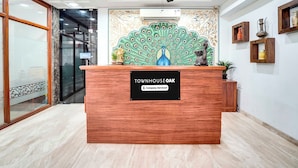 A reception desk with a 'TOWNHOUSE OAK' sign, a ceiling fan, and decorative wall art. - Townhouse Oak Durgapura Railway Junction (Jaipur)