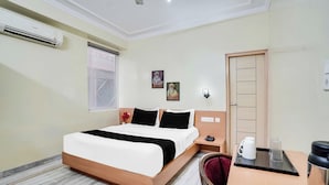 A hotel room with a bed, bedside table, a desk with a chair, a window, and a door. - Townhouse Oak Durgapura Railway Junction (Jaipur)