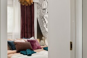 A bedroom with a bed, pillows, a window with blinds, and a wall with a black and white abstract design. - Laponia | Colourful Nordic Home with Private Sauna (Rovaniemi)