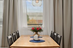 A dining table with chairs, a vase of flowers, and a window with blinds. - Laponia | Colourful Nordic Home with Private Sauna (Rovaniemi)