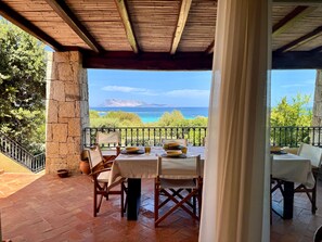 A covered outdoor dining area with a table set for two, overlooking a scenic view of the sea and mountains. - Villa Elena with Sea View, Terrace and Private Garden (San Teodoro)