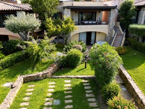 A courtyard with a stone pathway, lush greenery, and a building with a balcony. - Villa Elena with Sea View, Terrace and Private Garden (San Teodoro)