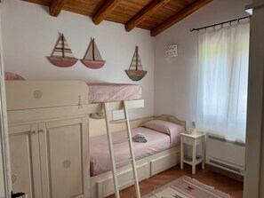 A bedroom with a bunk bed, a small bedside table, a heater, and a window with curtains. - Villa Elena with Sea View, Terrace and Private Garden (San Teodoro)
