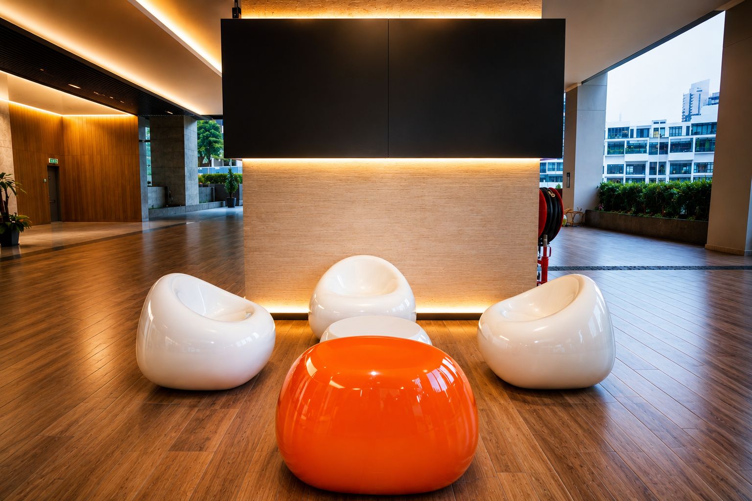 A modern lobby with a reception desk, wooden flooring, and three seating areas with white and orange chairs.