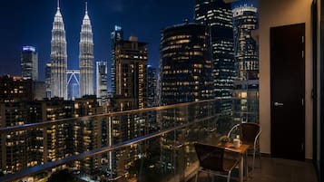 A balcony with a view of the Petronas Twin Towers and other city buildings at night.