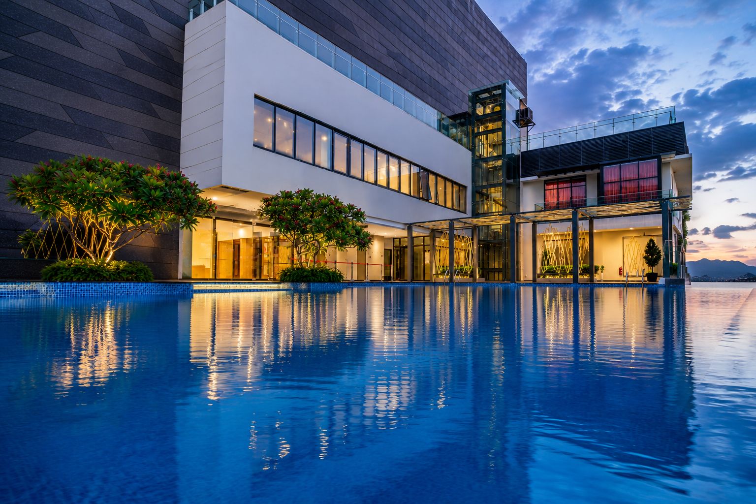 A modern hotel with a pool, large windows, and a view of the mountains.