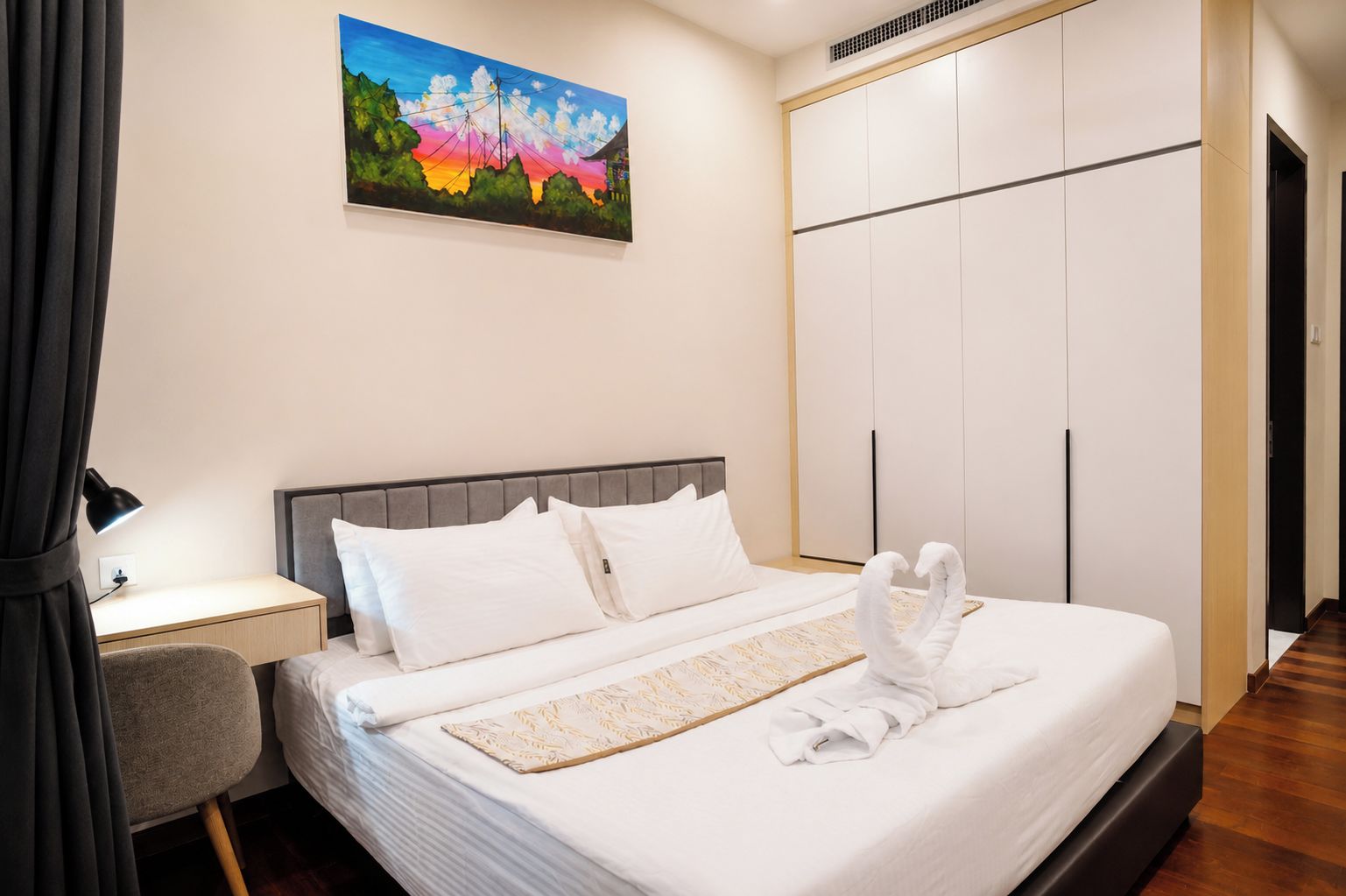 A hotel room with a bed, a desk, a chair, a wardrobe, and a painting on the wall.