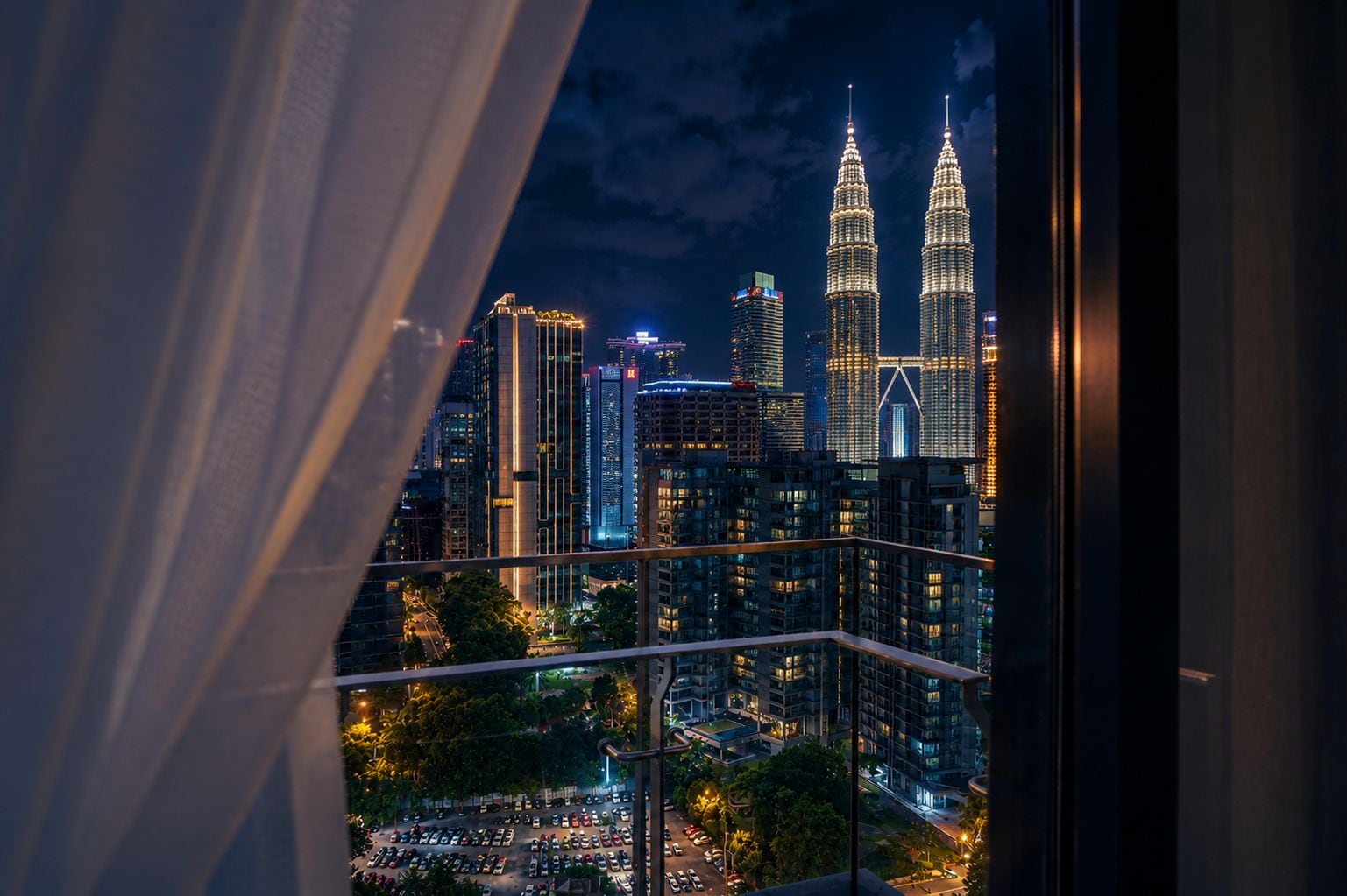 A nighttime cityscape with prominent skyscrapers, including two illuminated towers, through a window with a curtain.