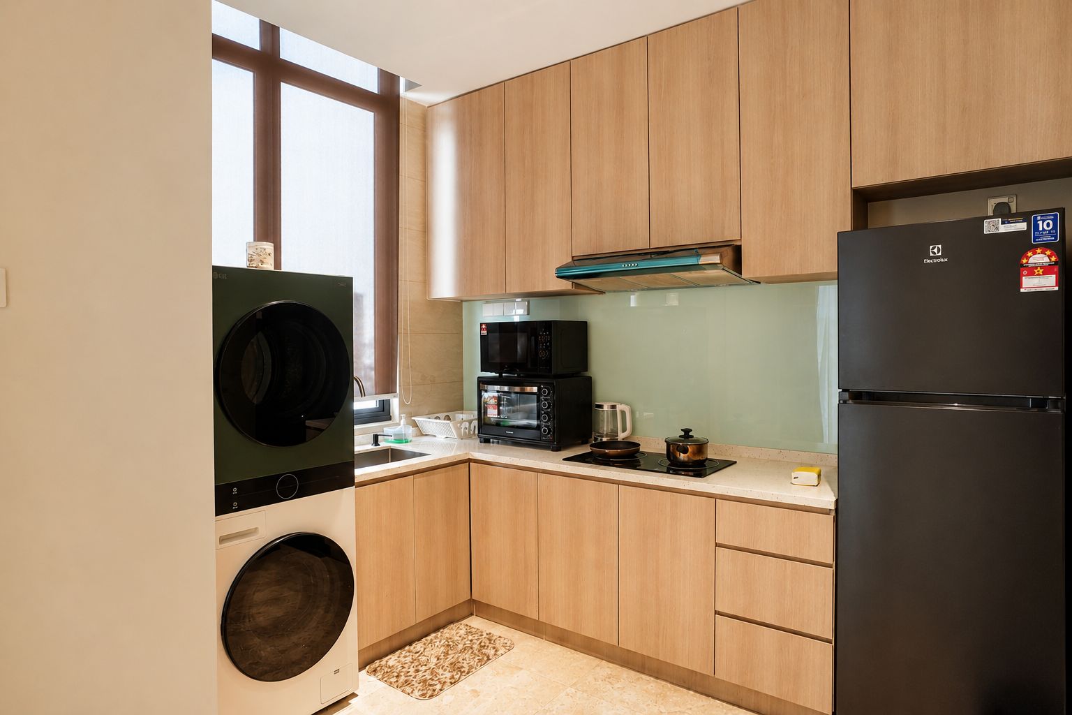 A compact kitchen with wooden cabinets, a black refrigerator, a microwave, a coffee maker, and a washing machine.