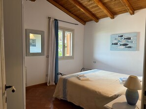 Ein Schlafzimmer mit einem Bett, einer Nachttischlampe, einem Fenster mit Vorh ängen, einem Wandbild und einer Tür.