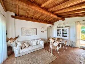 Ein gemütliches Wohnzimmer mit Holzboden, einem weißen Sofa, einem Esstisch mit Stühlen und einer Kommode mit Geschirr.