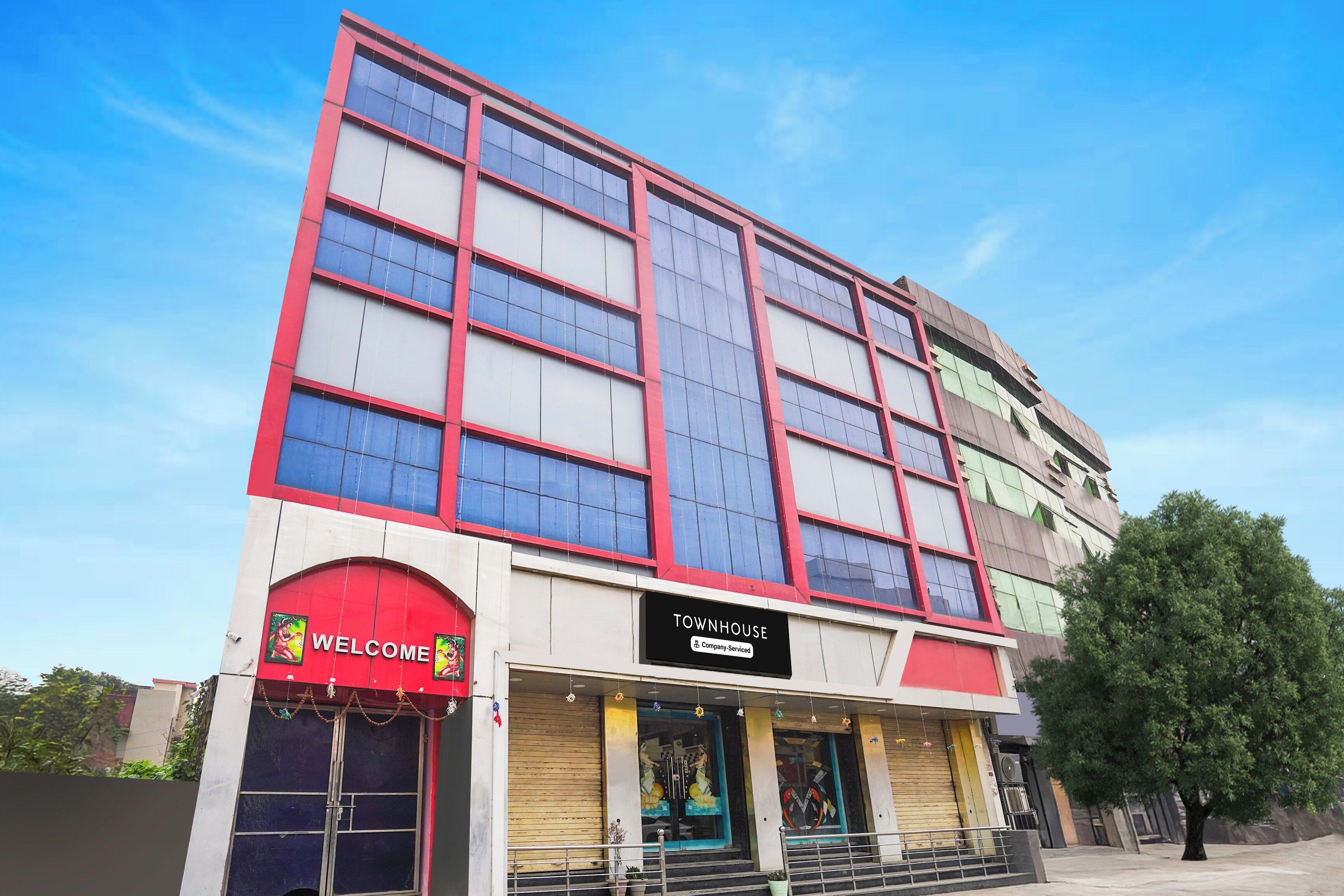 Un edificio de varios pisos con un llamativo letrero que dice 'WELCOME' y un letrero que indica 'TOWNHOUSE', señalando una propiedad de servicios empresariales.