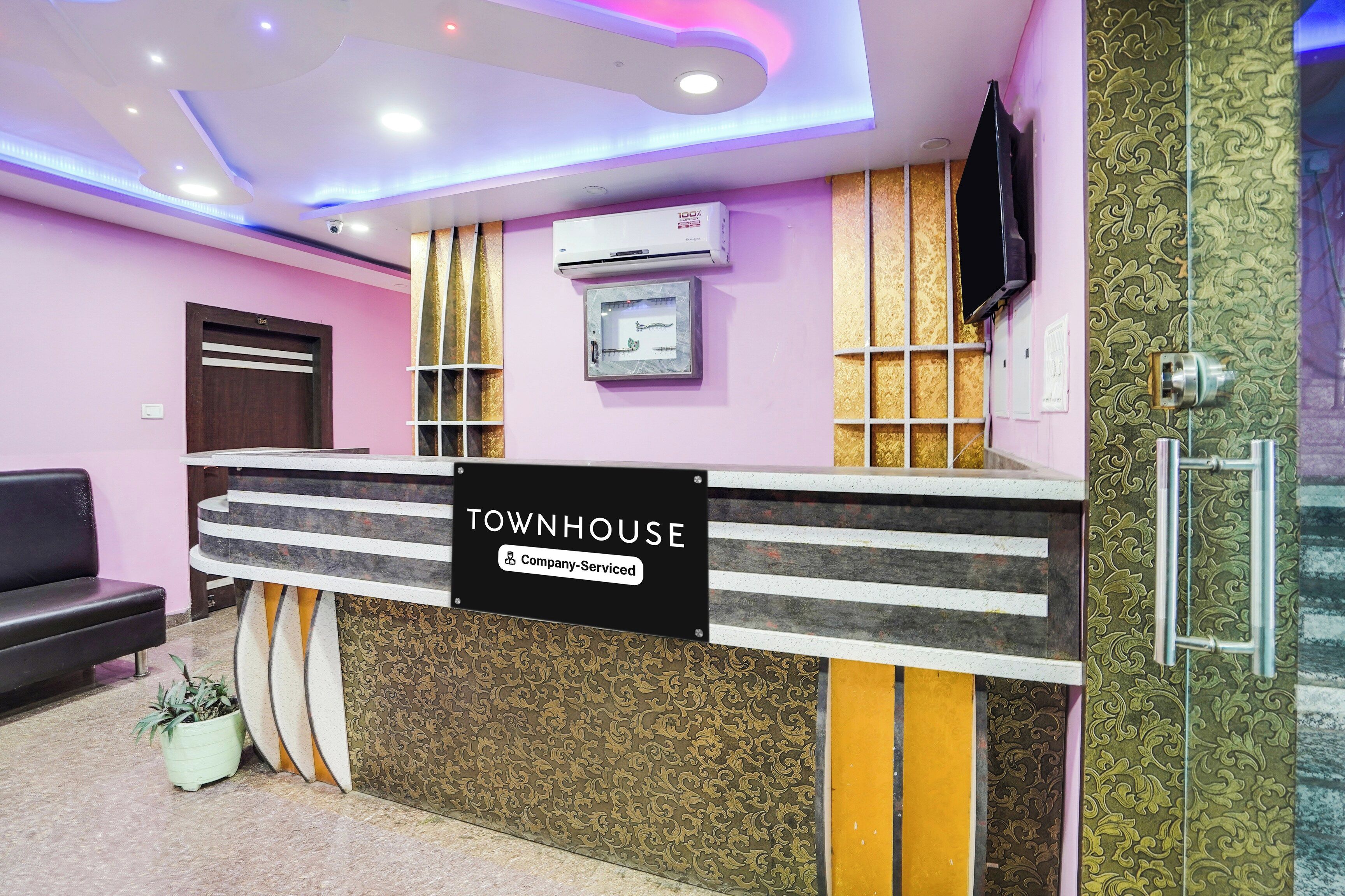 A reception desk with a sign indicating it is company-serviced, a mounted air conditioner, a television on the wall, and a patterned wall design.