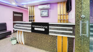 A reception desk with a sign indicating it is company-serviced, a mounted air conditioner, a television on the wall, and a patterned wall design.