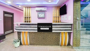 A reception desk with a sign indicating it is company-serviced, a mounted air conditioner, and a staircase to the right. - Townhouse Butler Road Near Maripur Chowk (Muzaffarpur)