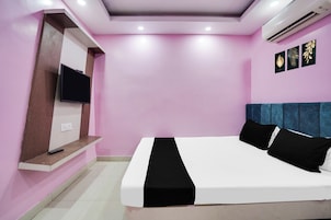 A bedroom with a bed, a TV mounted on a wall, and a ceiling air conditioner.
