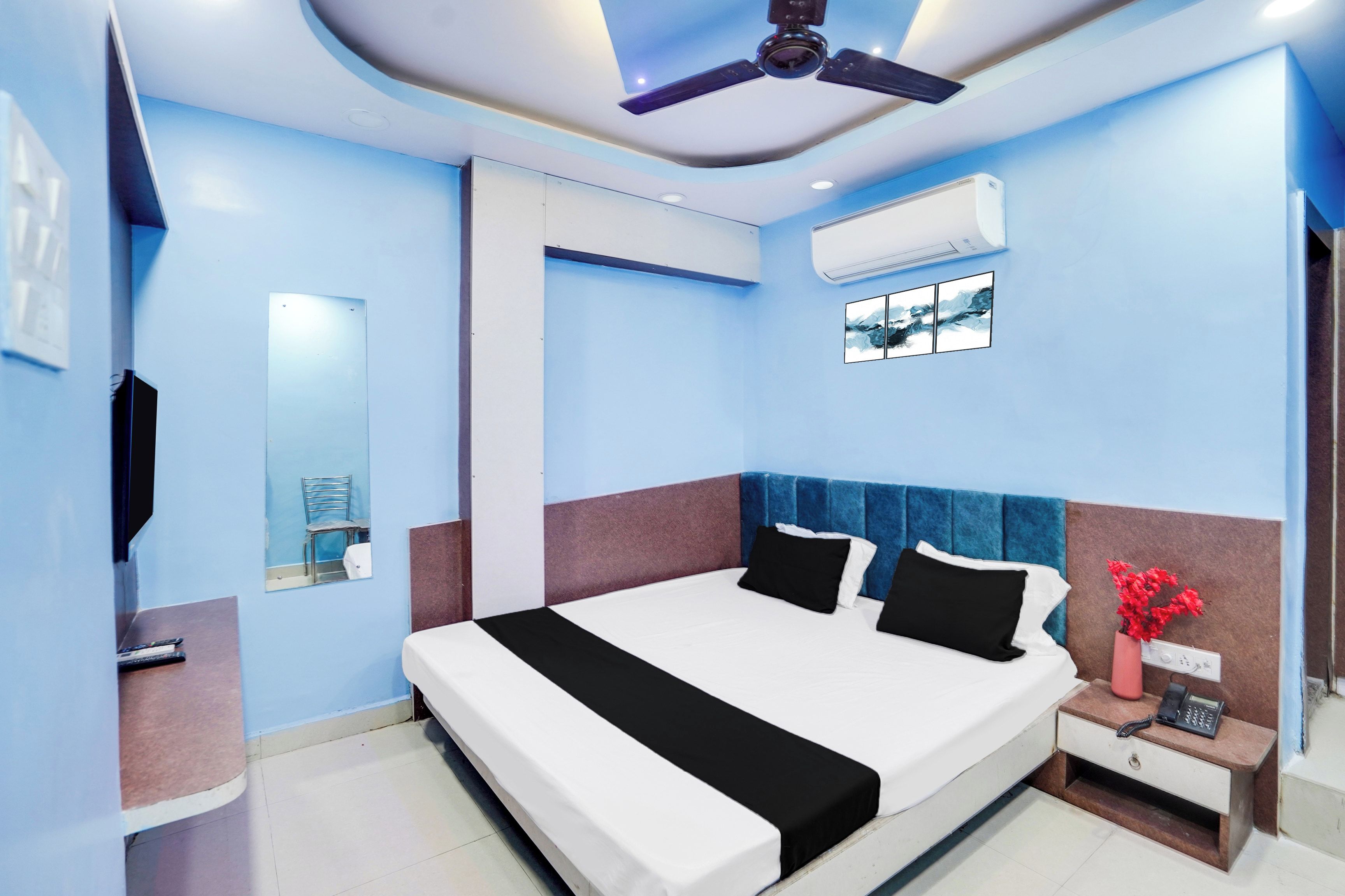 Une chambre d’hôtel avec un grand lit, un ventilateur de plafond, un appareil de climatisation, une petite table de chevet avec un téléphone et un miroir au mur.