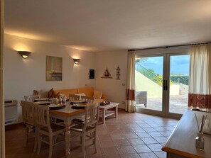 A dining area with a table and chairs, a sofa, and a view through a glass door to an outdoor area. - Villa Elena Ground Floor – Sea Front and Garden (San Teodoro)