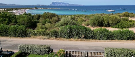 A coastal road with a view of the sea, boats, and a mountain in the distance.