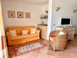 A living room with a sofa, a wicker chair, a flat-screen TV, a cabinet, and decorative wall art. - Villa Elena Ground Floor – Sea Front and Garden (San Teodoro)