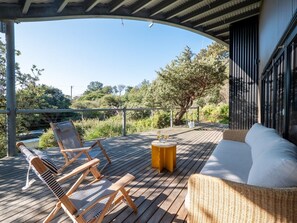 Eine Holzterrasse mit Gartenmöbeln, darunter ein Rattansofa und zwei gestreifte Lounge-Stühle.