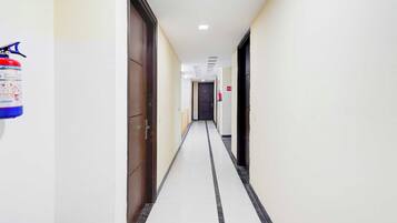 A corridor with doors on both sides, a fire extinguisher on the left, and a fire hose on the right.