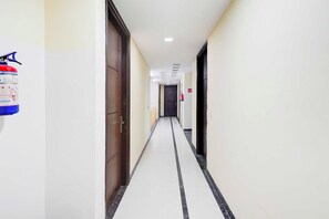 A corridor with doors on both sides, a fire extinguisher on the left, and a fire hose on the right. - Townhouse Oak Sector 51 Noida (Noida)