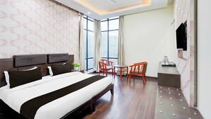 Een hotelkamer met een bed, een bureau, stoelen, een plafondventilator en een groot raam.