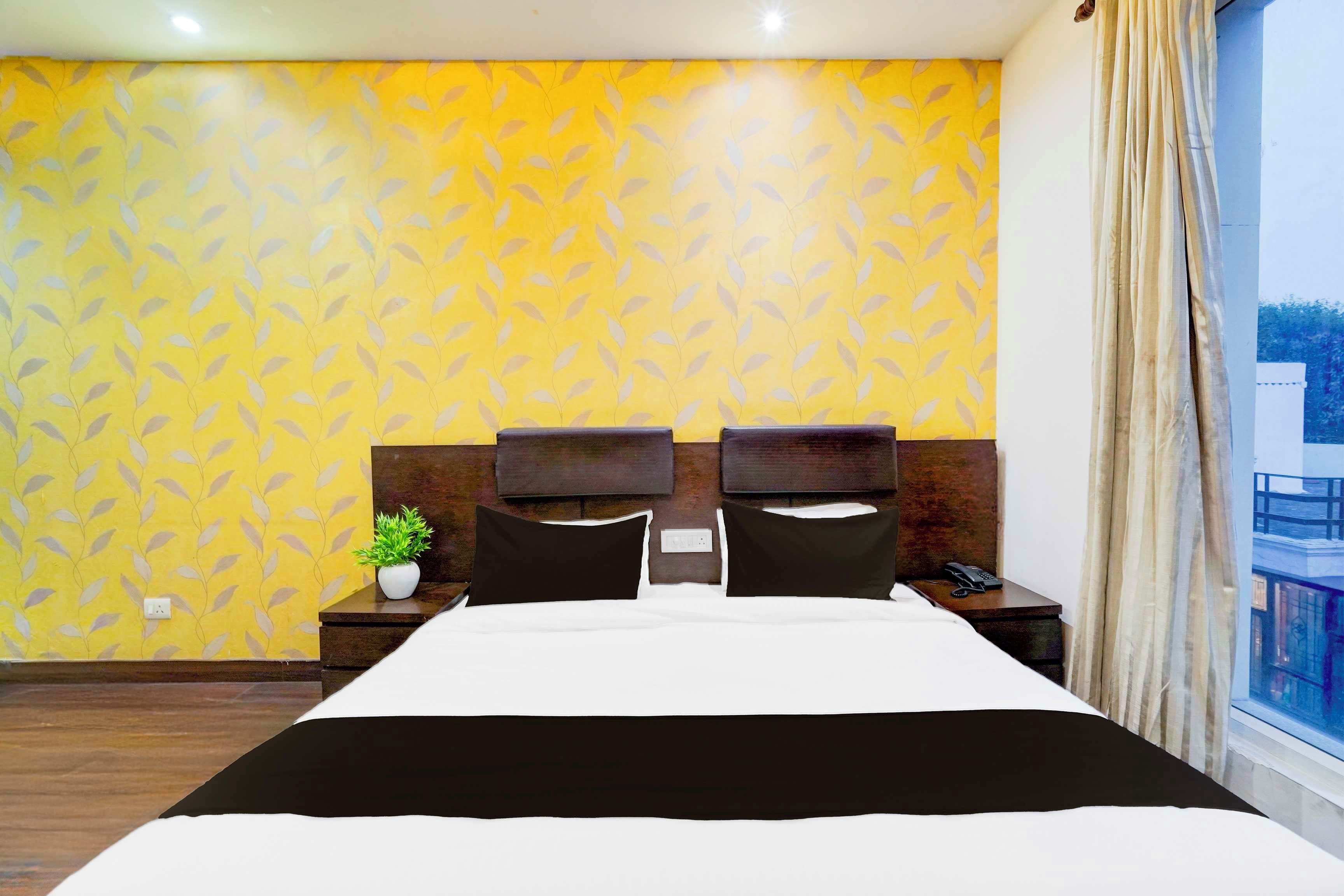 Una habitación de hotel con una cama grande, una mesita de noche con teléfono y una ventana con cortinas.