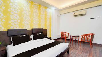 A hotel room with a bed, two chairs, a small table, an air conditioning unit, and a wall with a floral pattern.