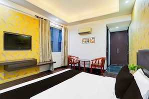 Una habitación de hotel con una cama, televisión, escritorio, dos sillas, aire acondicionado y una puerta que da a otra habitación.