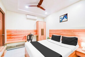 Una habitación de hotel con una cama, un escritorio, una silla, un armario, un ventilador de techo, un cuadro en la pared y un equipo de aire acondicionado.
