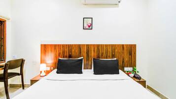 Une chambre d’hôtel avec une tête de lit en bois, un lit avec une literie blanche, une table de chevet avec une lampe et une petite plante en pot.