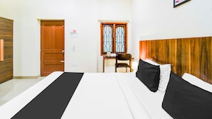 Hotellihuone, jossa on sänky, puinen pääty, työpöytä tuolilla ja ikkuna, jossa on sälekaihtimet.