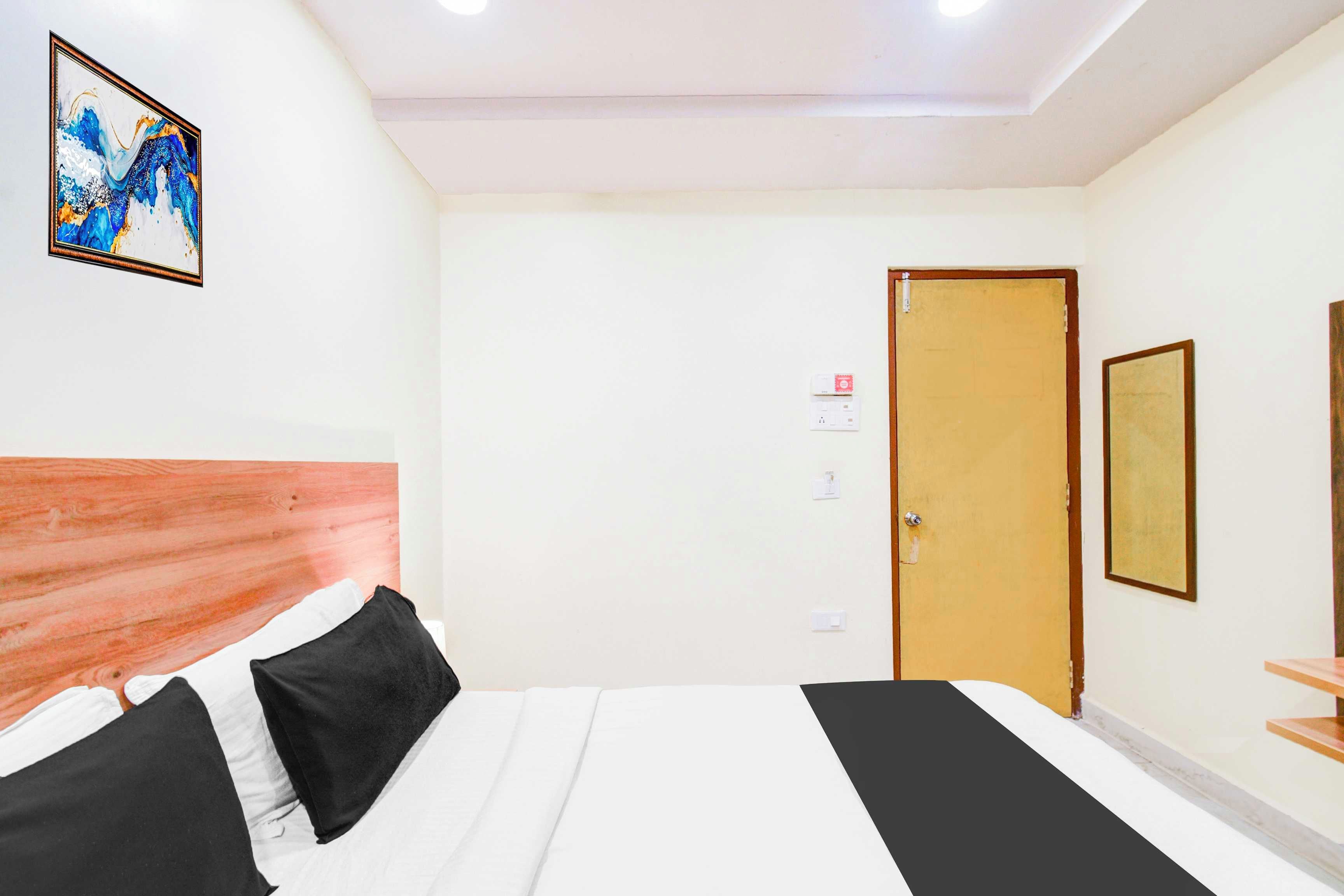 Habitación de hotel con cama, cabecera de madera, un cuadro en la pared, una puerta y una mesita.