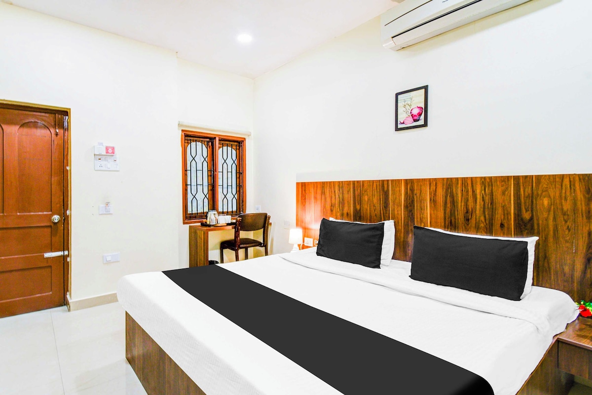 Habitación de hotel con cama, cabecera de madera, escritorio con silla, ventana con rejas y unidad de aire acondicionado.