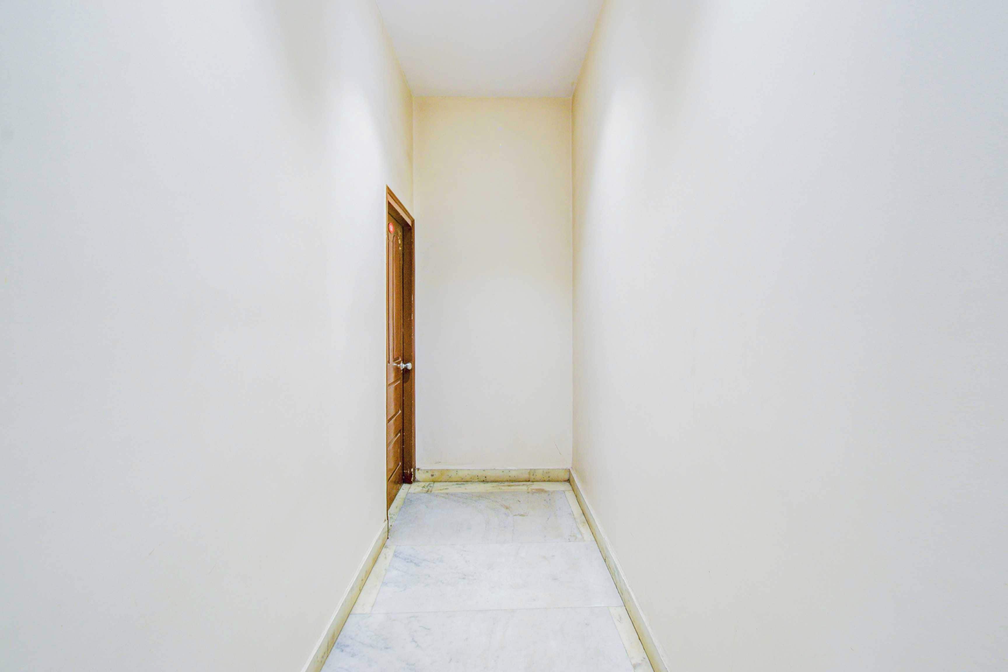 Un pasillo estrecho con una puerta de madera al final, paredes blancas y suelo de baldosas.