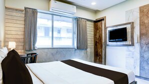 Hotellihuone, jossa on sänky, seinälle asennettu televisio ja ikkuna, jossa on verhot.