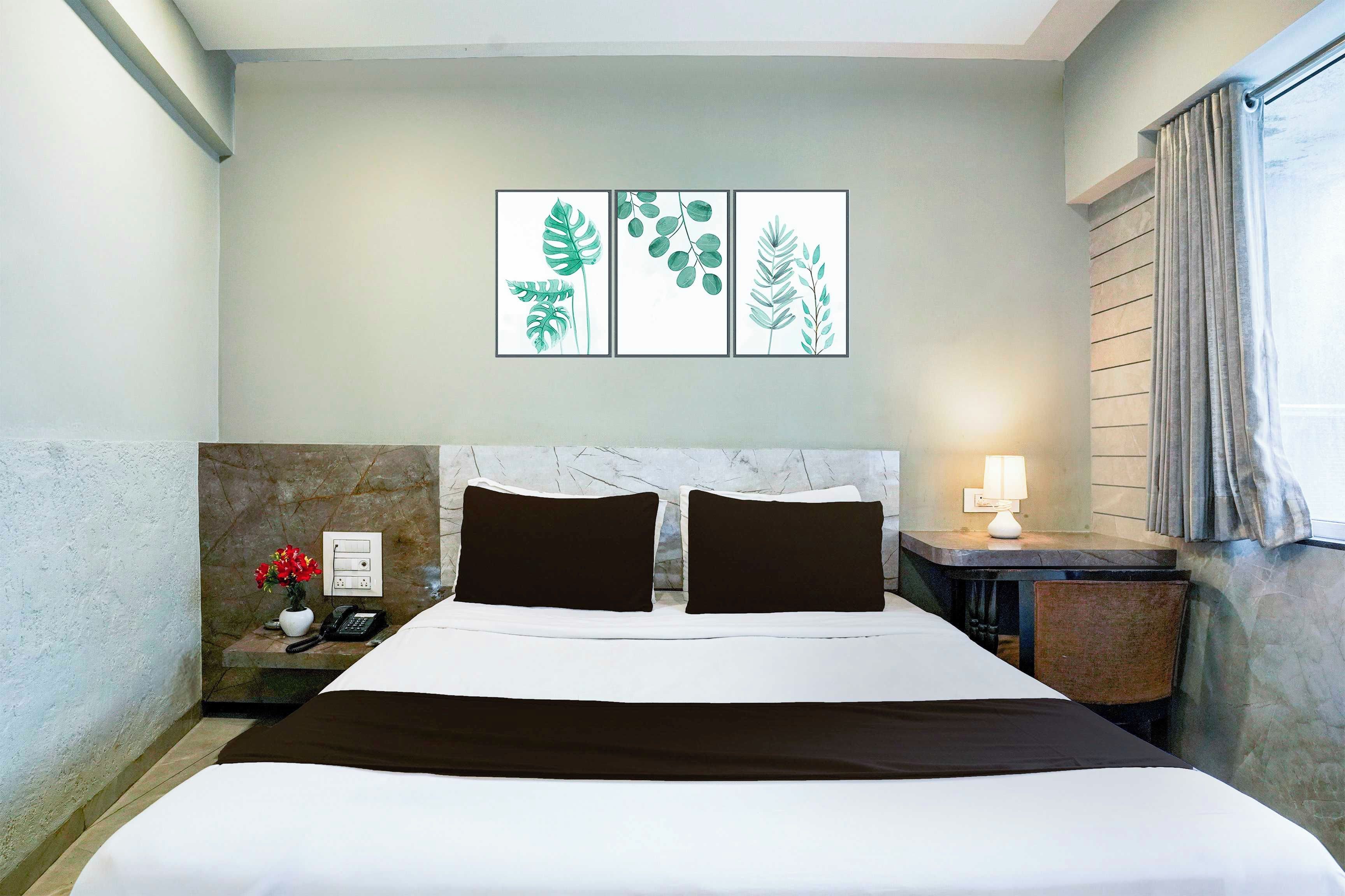 A hotel room with a marble headboard, a bed with white and brown bedding, a nightstand with a phone and a vase of flowers, and a wall with three framed botanical prints.
