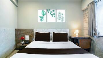 A hotel room with a marble headboard, a bed with white and brown bedding, a nightstand with a phone and a vase of flowers, and a wall with three framed botanical prints.