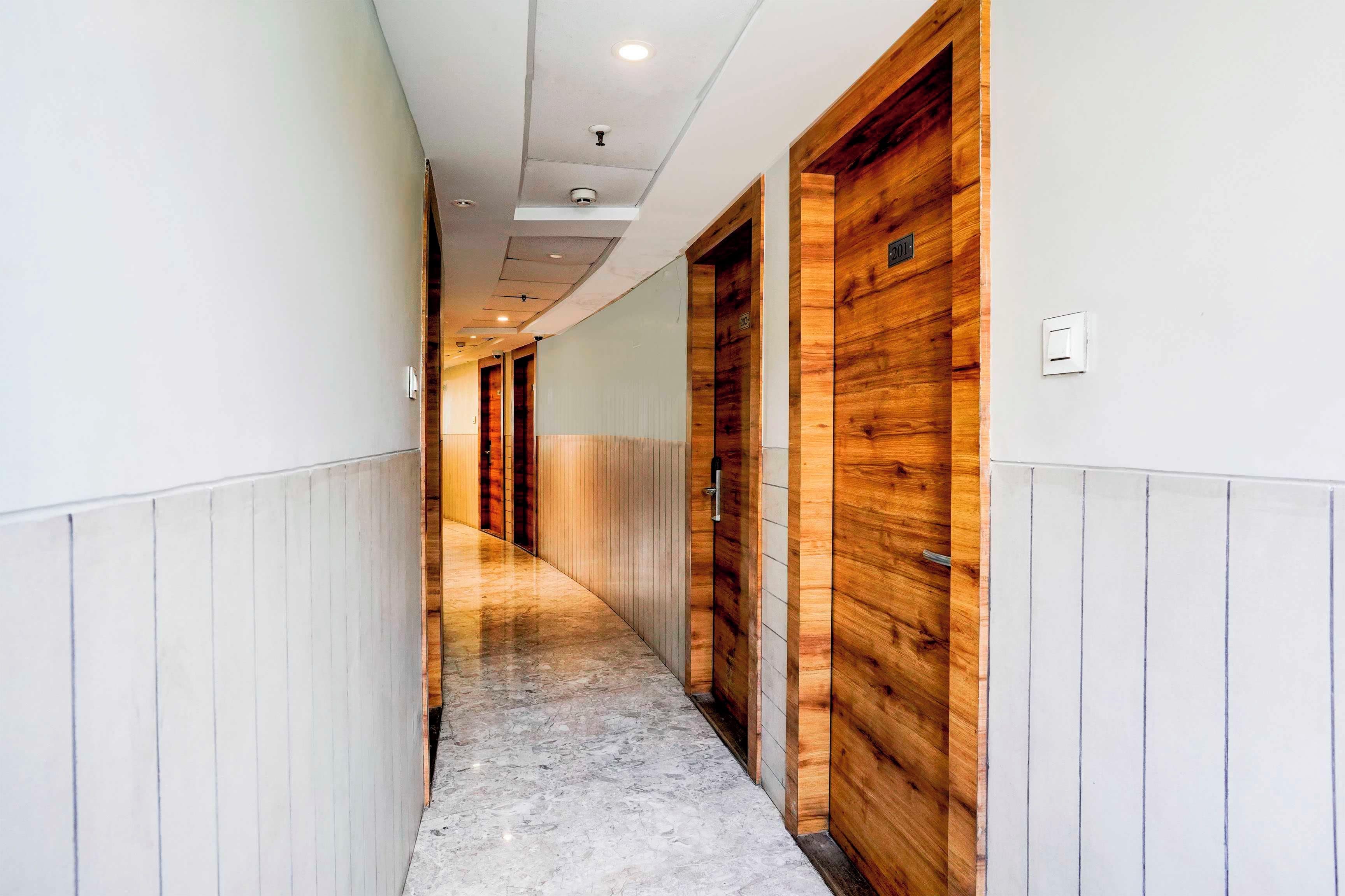 A corridor with wooden doors, white walls, and a marble floor.