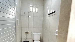 Casa de banho pequena com azulejos, vaso sanitário, chuveiro e secador de mãos.