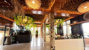 Um hall amplo com uma mesa de recepção, pilares de pedra e uma grande janela que permite entrada de luz natural.