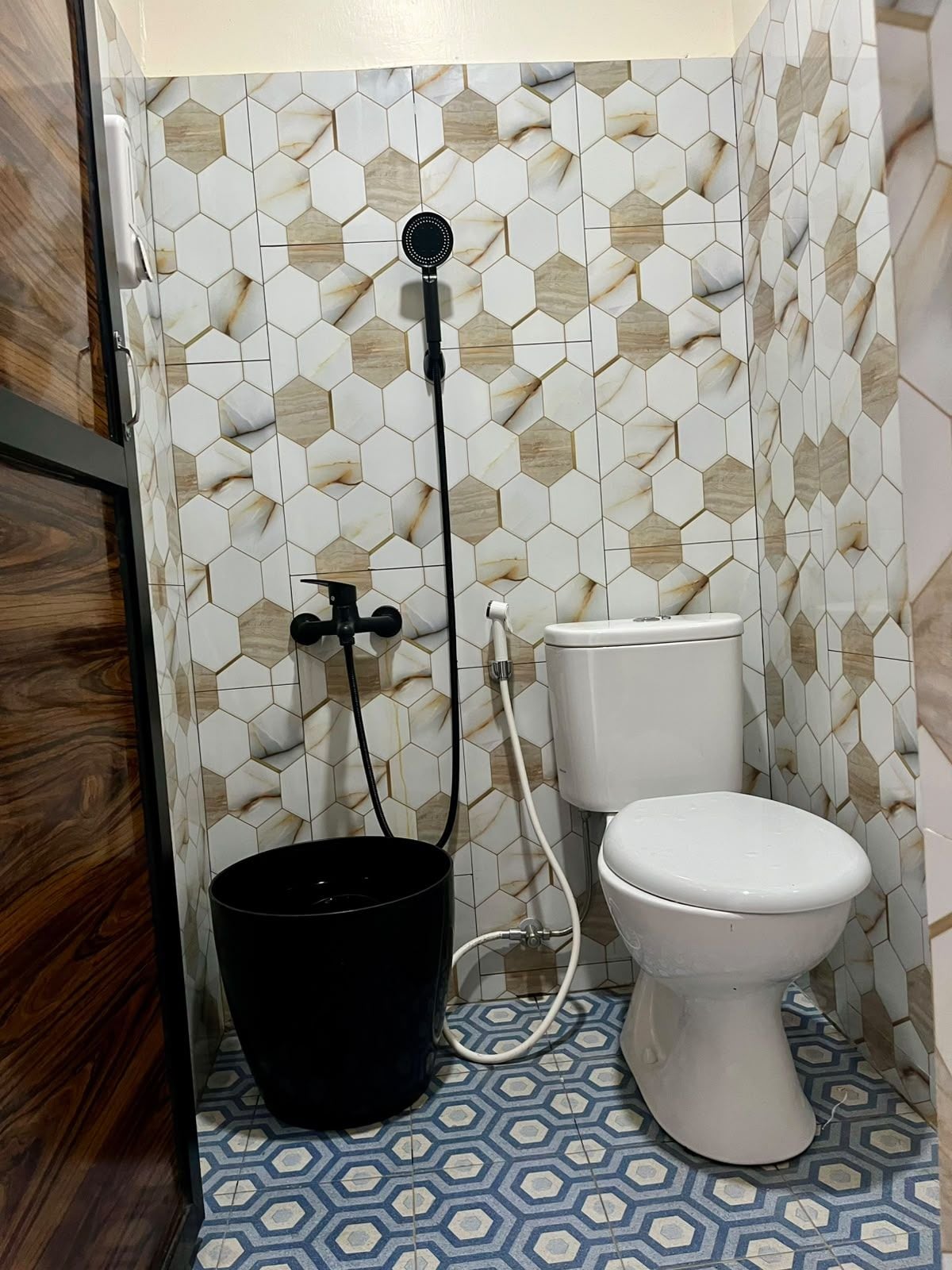 A bathroom with a toilet, a black bucket, and a shower head.
