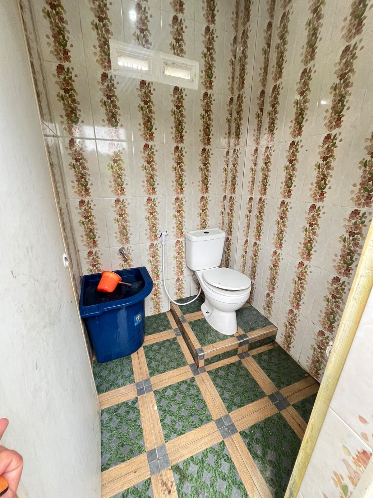 Un baño pequeño con inodoro, un cubo de basura azul y baldosas estampadas en las paredes y el suelo.
