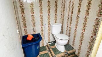 Un baño pequeño con inodoro, un cubo de basura azul y baldosas estampadas en las paredes y el suelo.